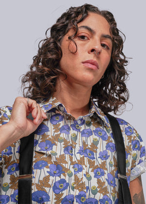 S=Person wearing a floral shirt with blue flowers and suspenders against a plain background