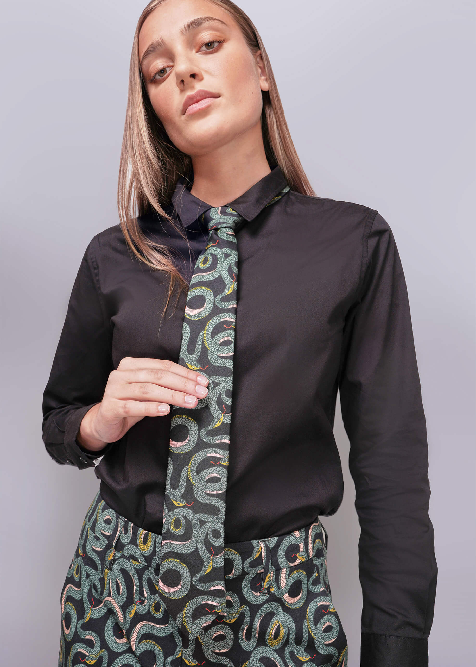 Woman wearing a black shirt with a patterned tie and skirt against a light gray background