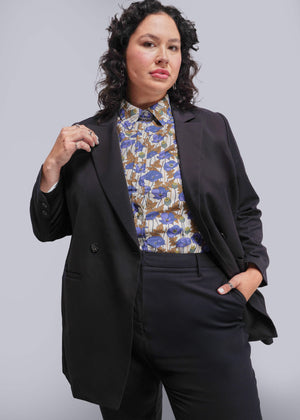 1X=Person wearing a black suit with a floral blouse against a plain background