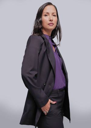 1X=Person wearing a black blazer over a purple shirt against a light gray background