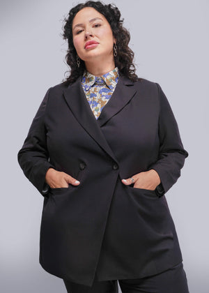 1X=Person wearing a black blazer over a patterned shirt on a plain background