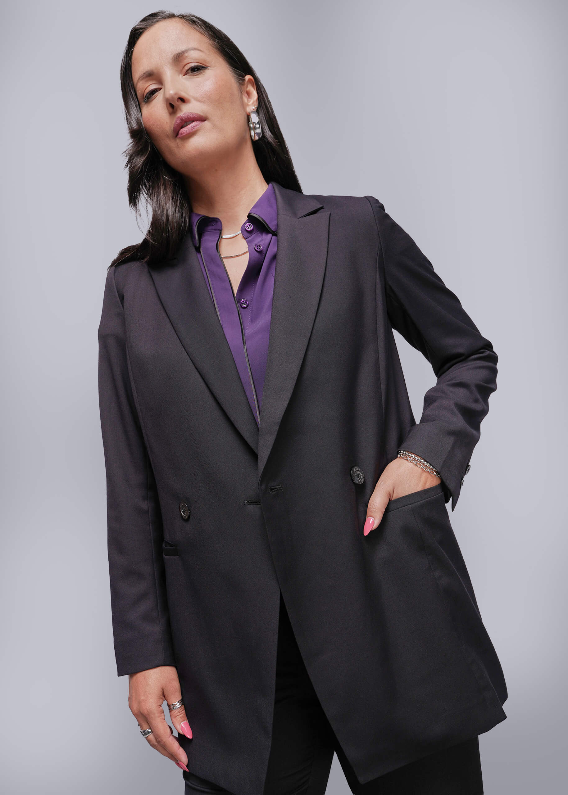 S=Woman wearing a black blazer over a purple shirt against a gray background