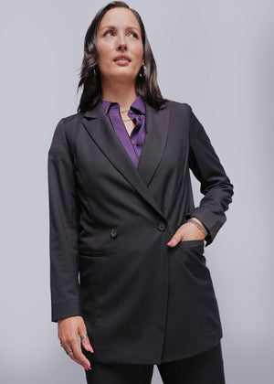 S=Woman wearing a black blazer over a purple shirt on a gray background