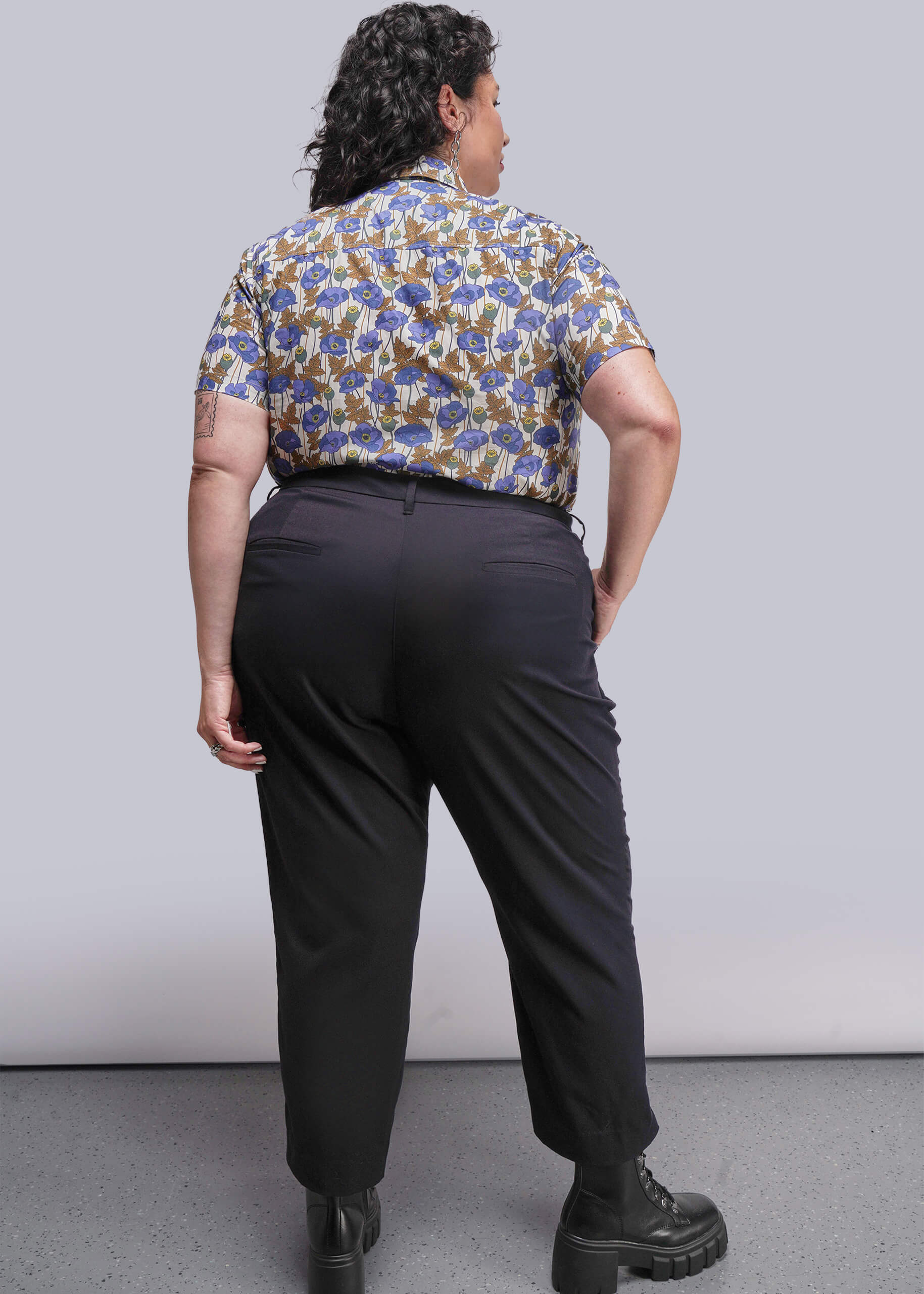 1X=Person wearing a patterned shirt and black pants against a plain background