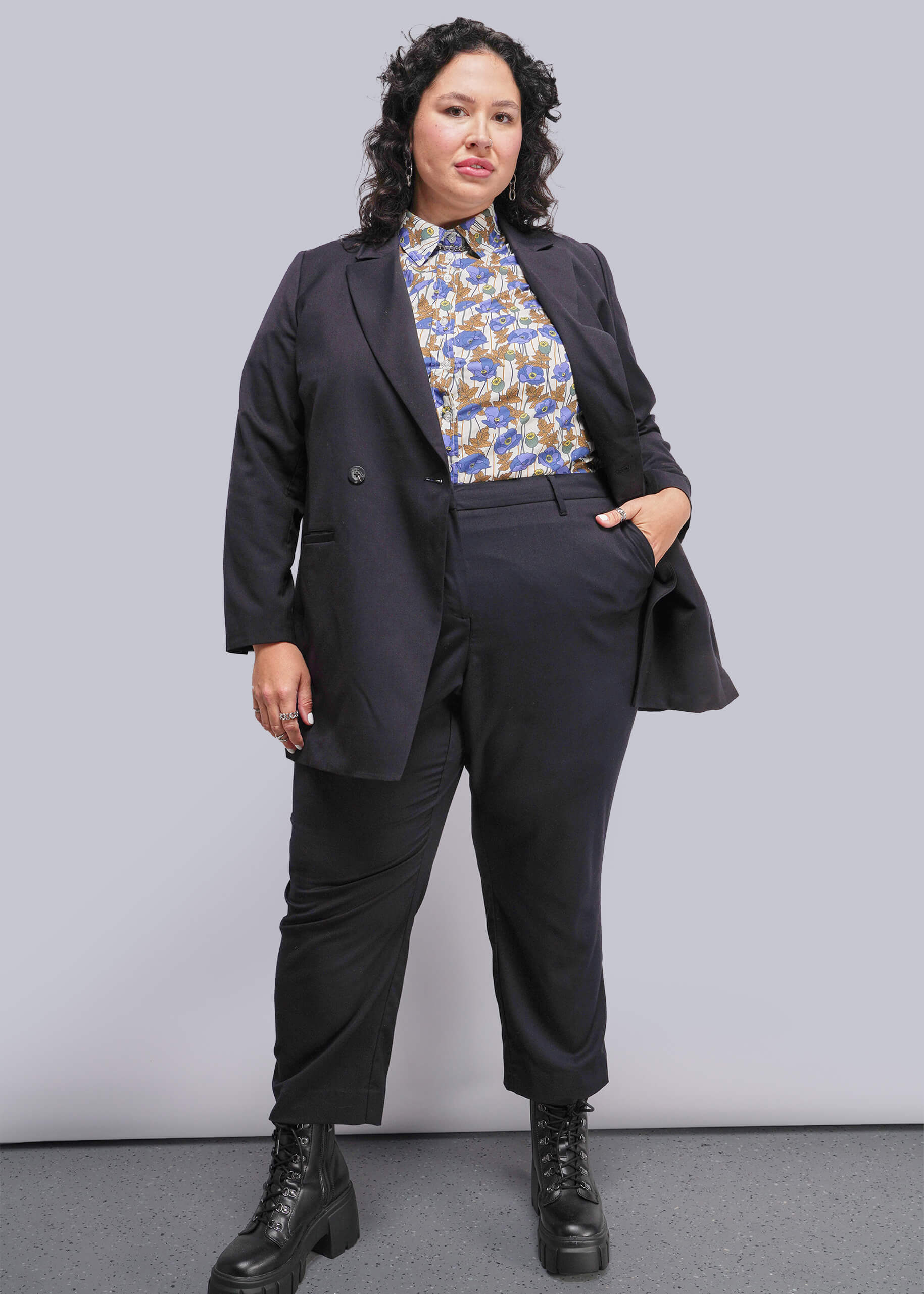 1X=Person wearing a black suit with a patterned blouse against a plain background