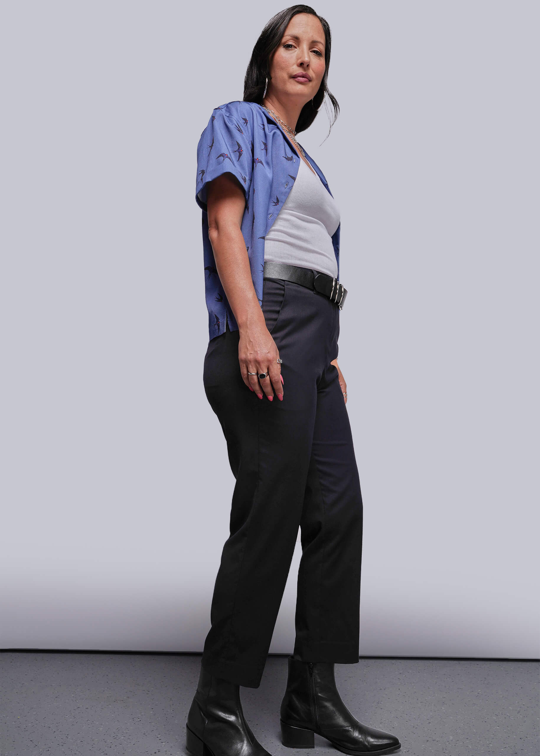 S=Woman wearing a blue shirt, white top, black pants, and black boots against a plain background