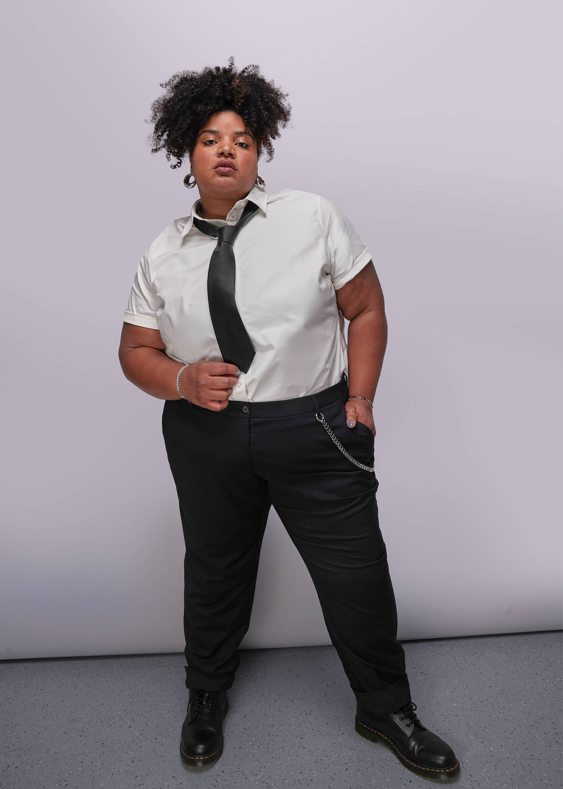 1X=Person wearing a white shirt, black tie, and black pants against a plain background