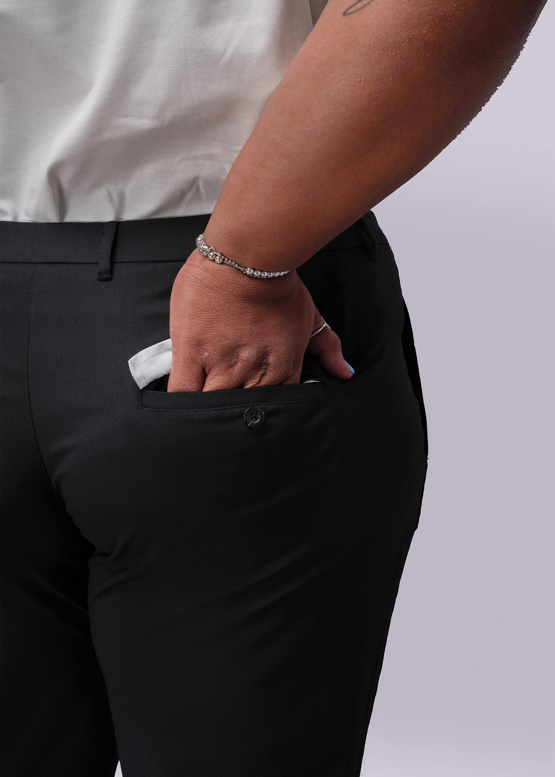 1X=Person wearing black pants with a white shirt, holding a white object in their pocket against a light gray background.