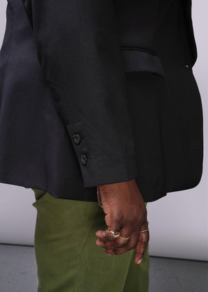 1X=Person wearing a black suit jacket and green pants with a white background