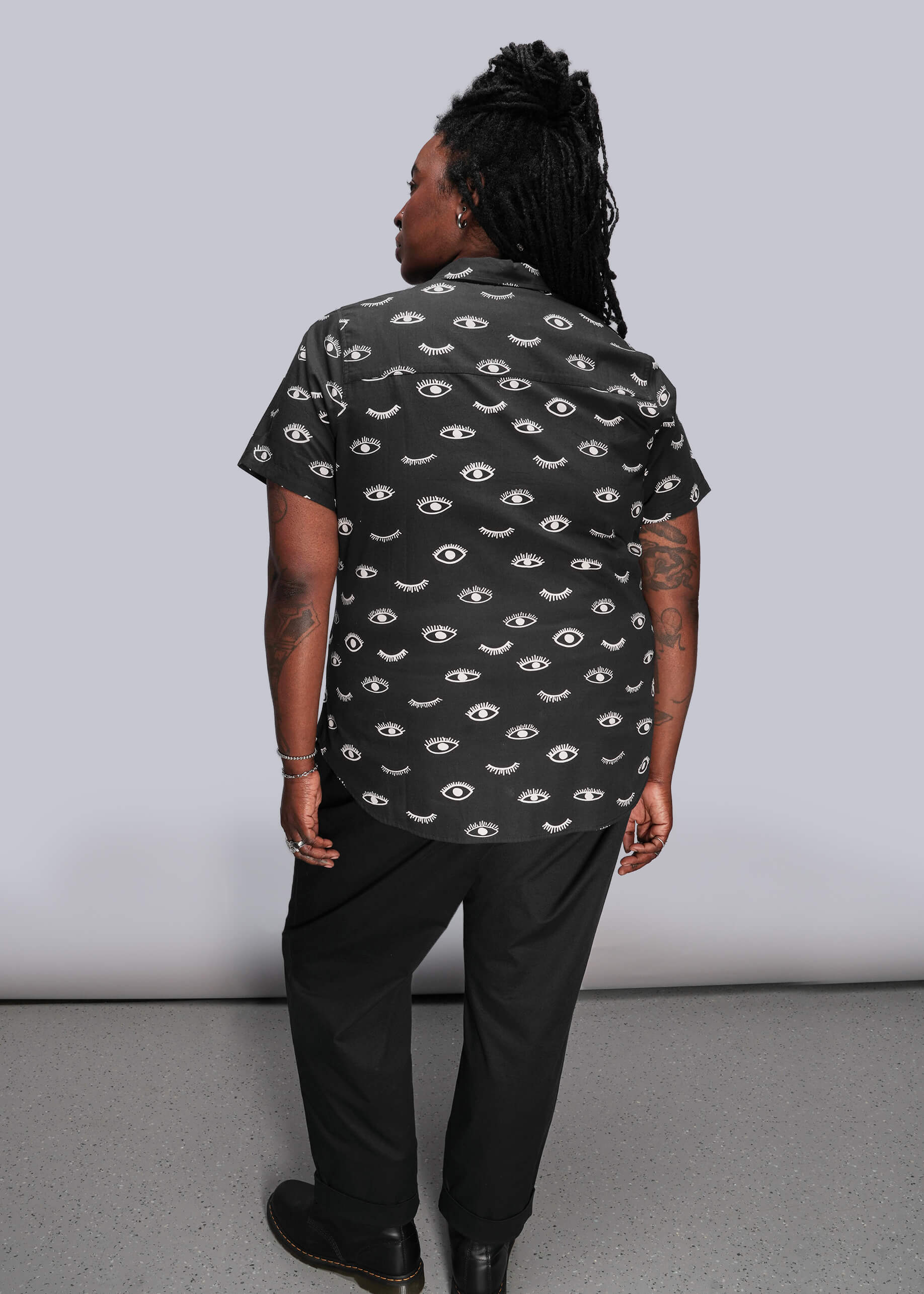 1X=Person wearing a black shirt with eye pattern against a plain background