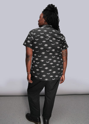1X=Person wearing a black shirt with eye pattern against a plain background