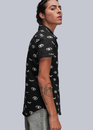 S=Person wearing a black short-sleeve shirt with eye pattern on a gray background