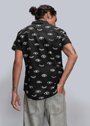 S=Person wearing a black short-sleeve shirt with eye pattern on a plain background