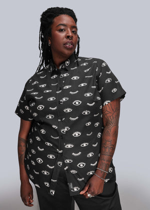 1X=Person wearing a black shirt with eye pattern against a gray background