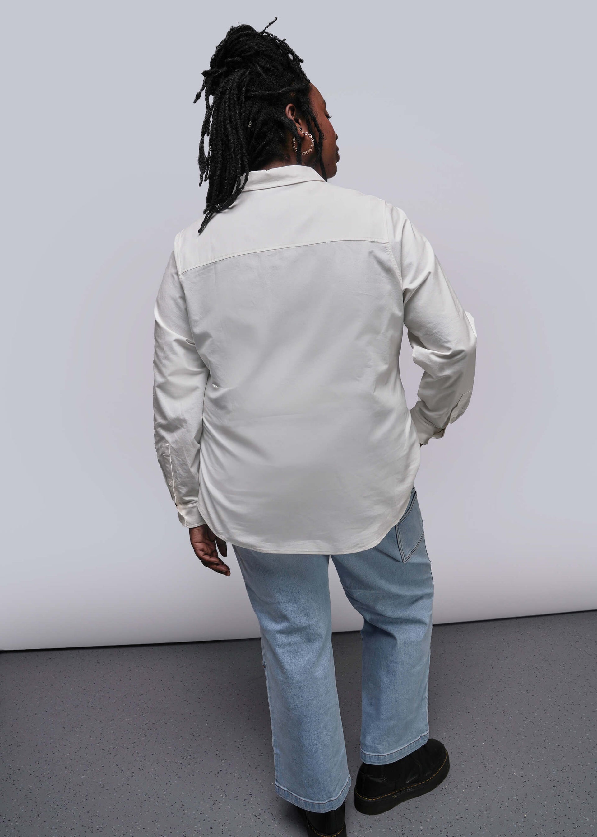 1X=Person wearing a light-colored shirt and jeans from behind on a plain background