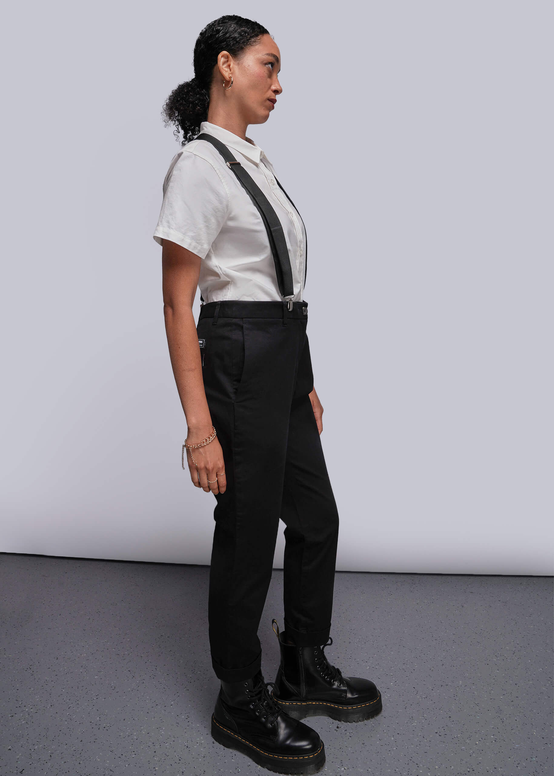 S=Person wearing a white shirt, black suspenders, black pants, and black boots on a plain background