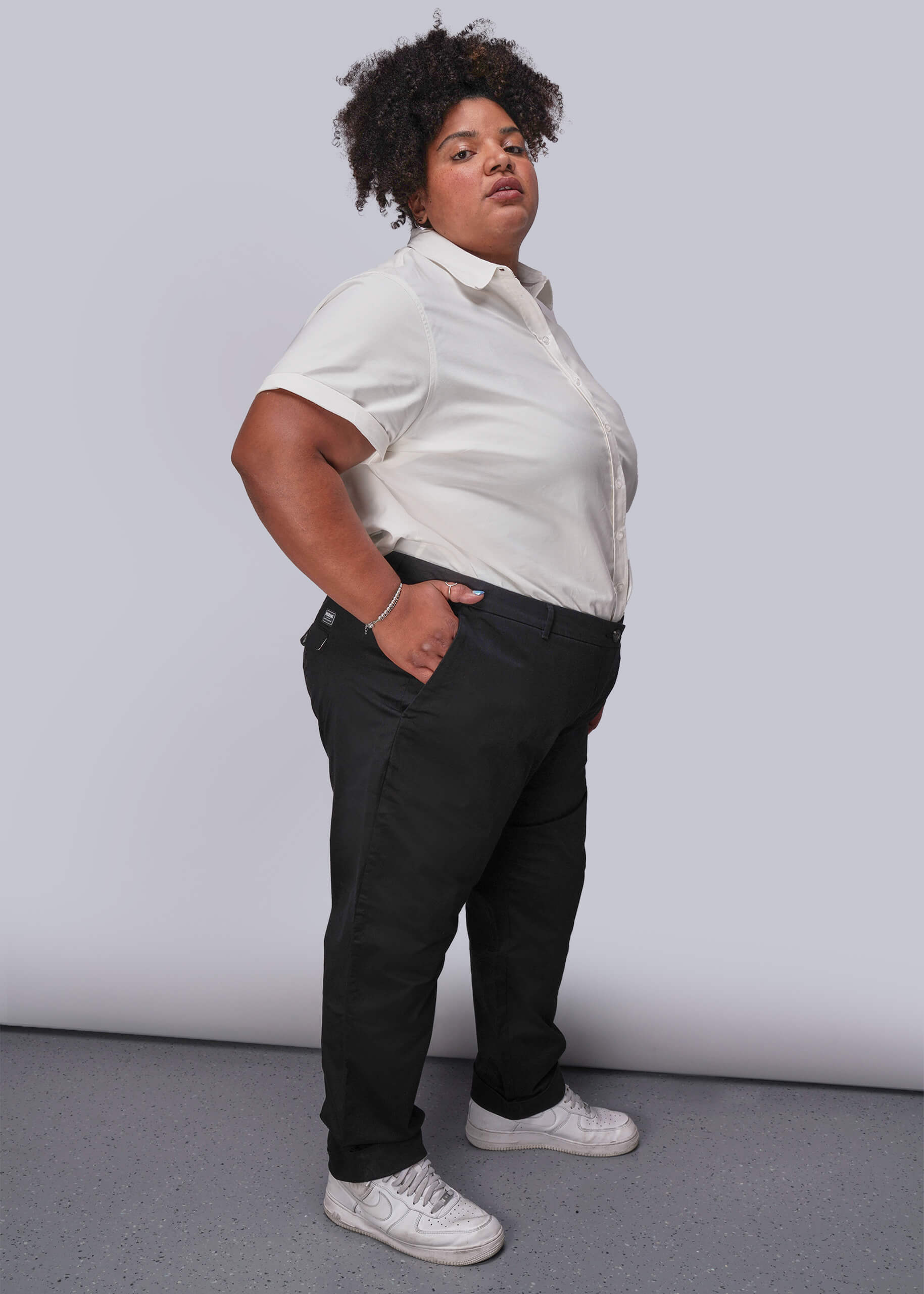 1X=Person wearing a white button up shirt and black pants against a plain background