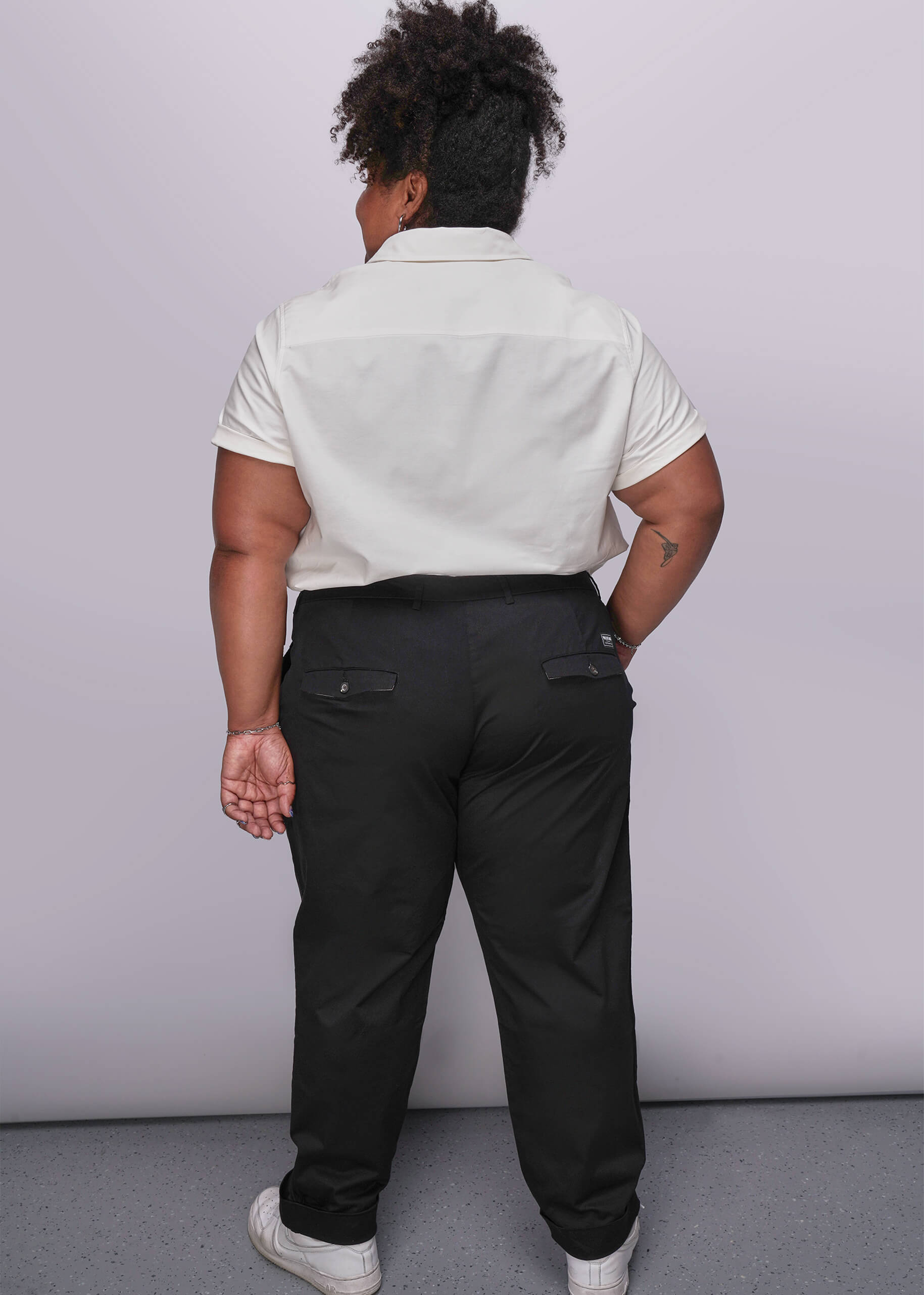 1X=Person wearing a white shirt and black pants against a plain background