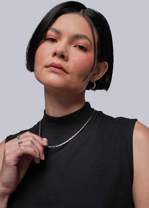 S=Person wearing a black sleeveless top and silver necklace against a light gray background