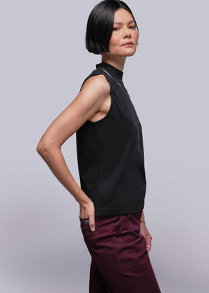 S=Person wearing a black sleeveless top and maroon pants against a light gray background