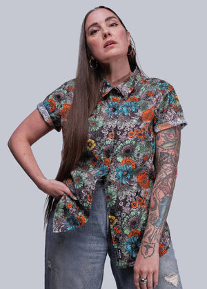 S=Woman wearing a colorful floral shirt against a plain background