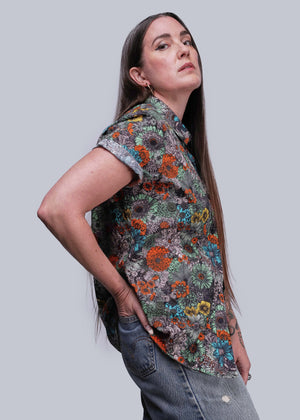 S=Woman wearing a colorful floral shirt against a gray background