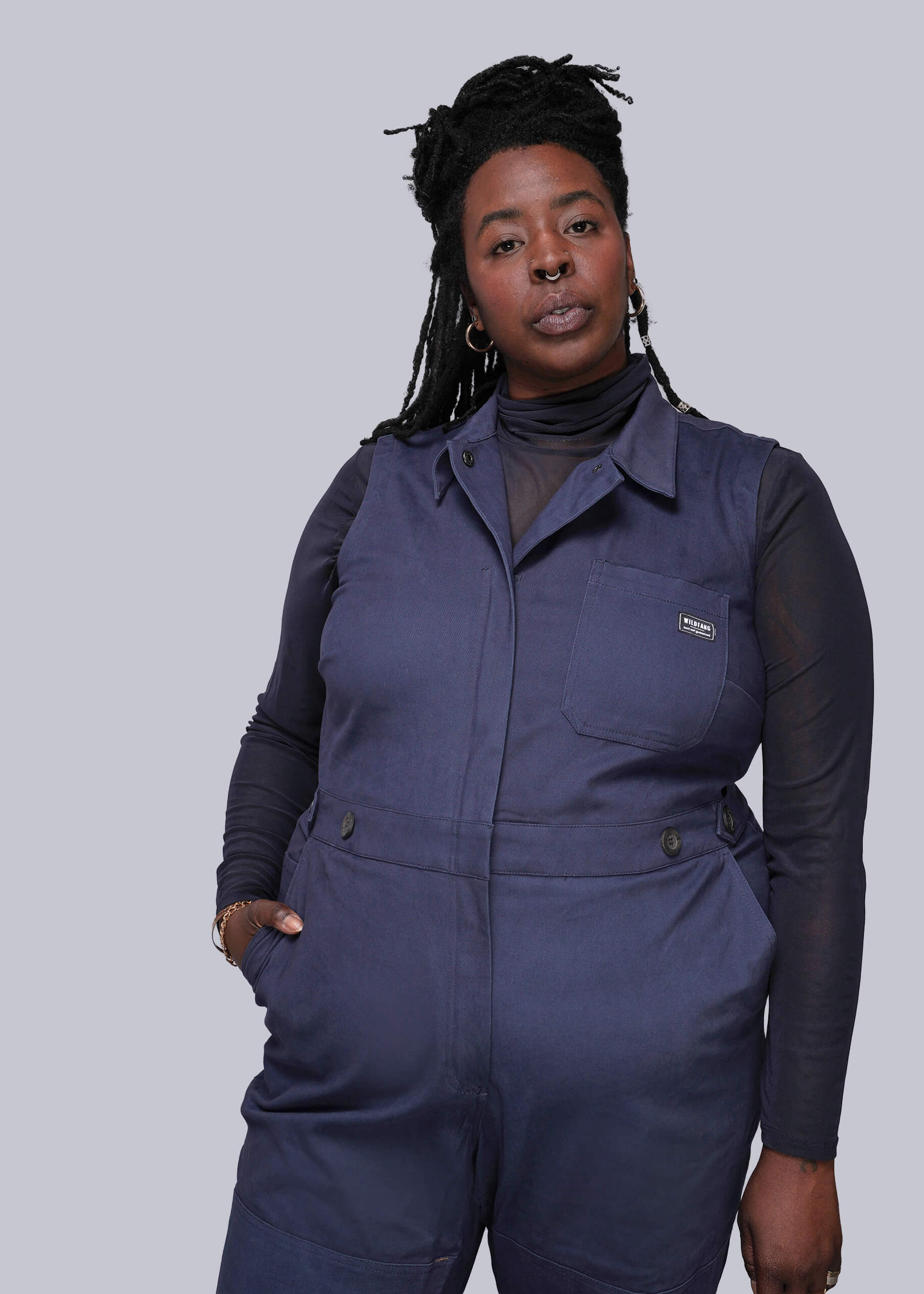 1X=Person wearing a blue coverall over a black long-sleeve shirt on a plain background