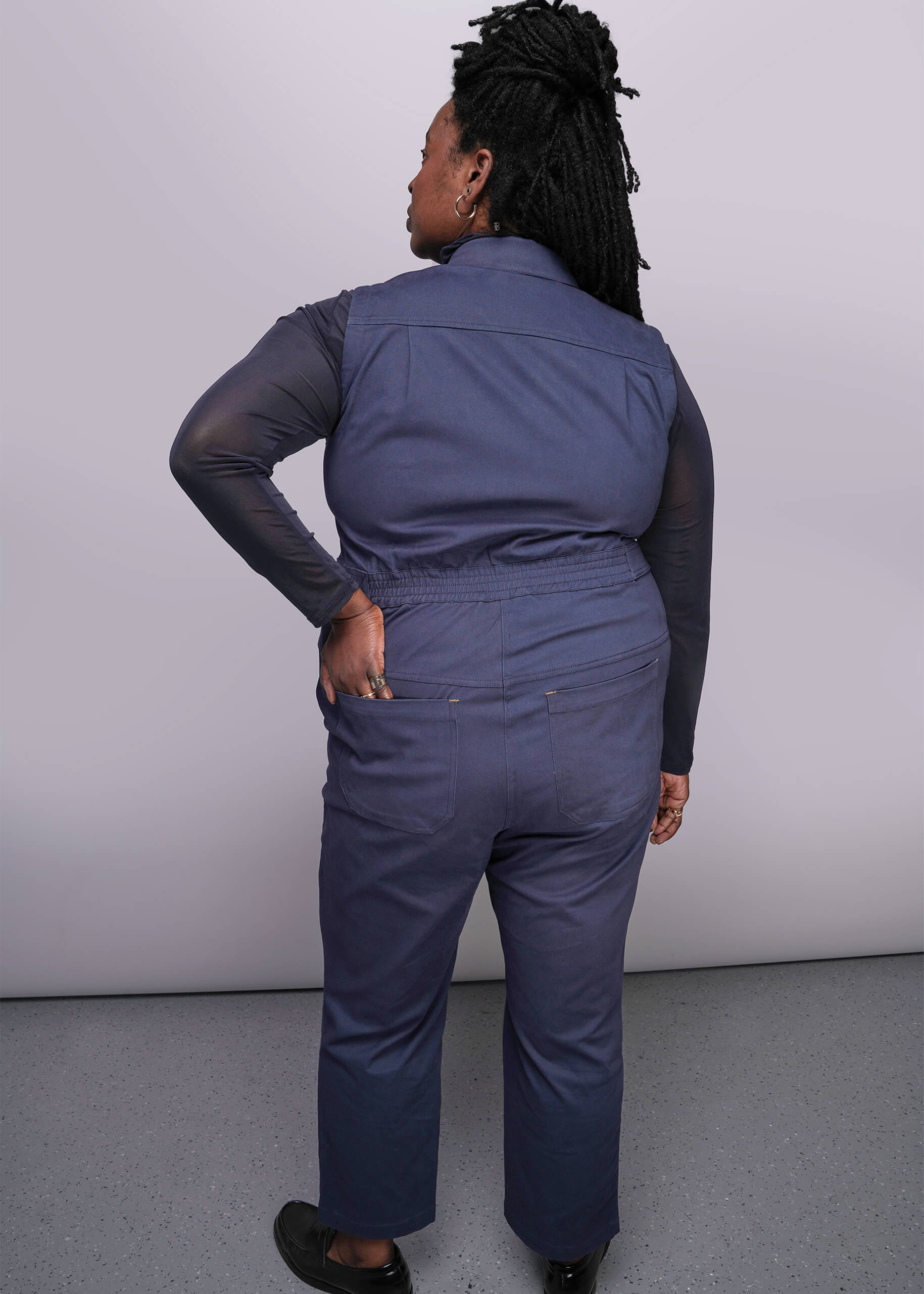 1X=Back of person wearing a navy blue jumpsuit against a plain background