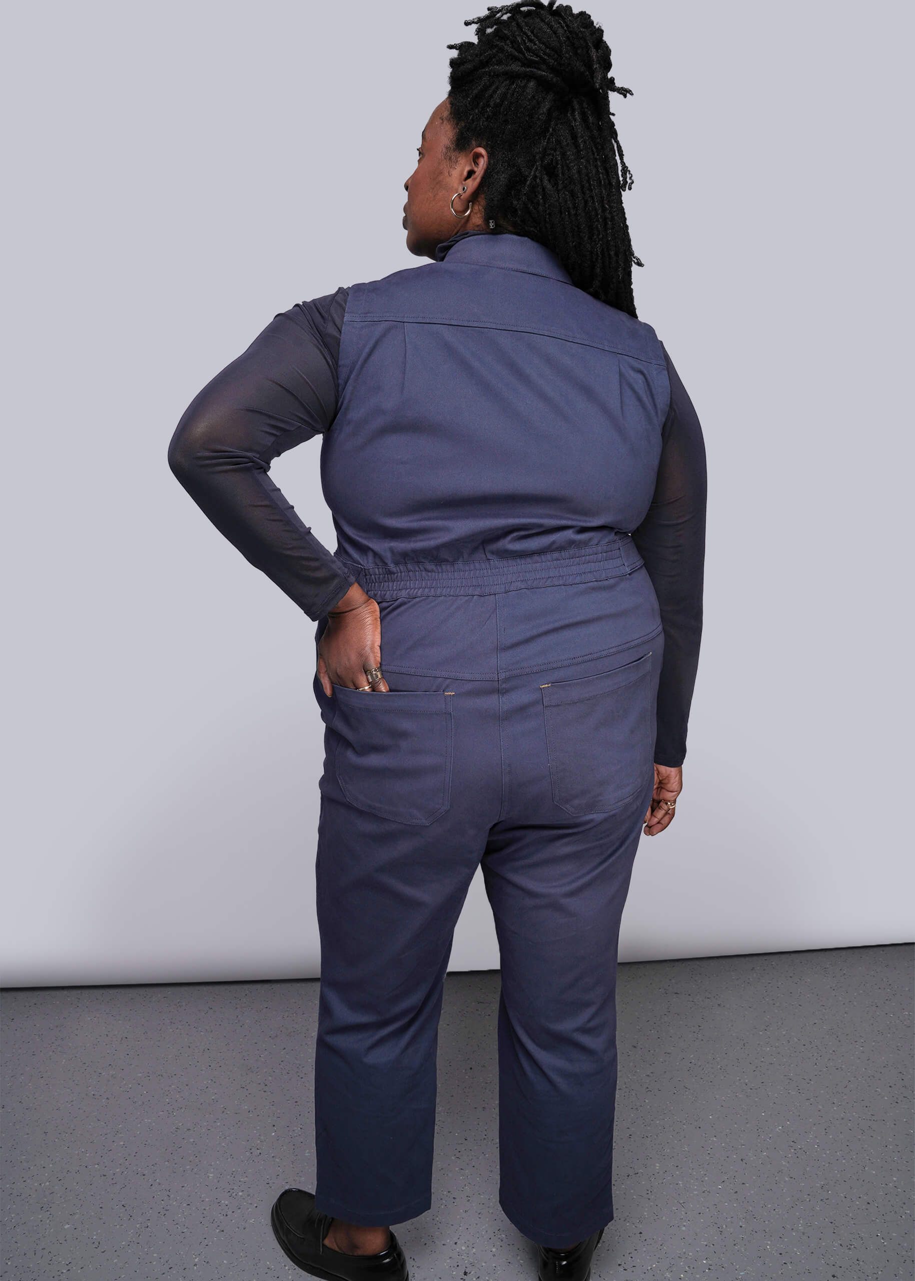 1X=Back of person wearing a navy blue jumpsuit against a plain background