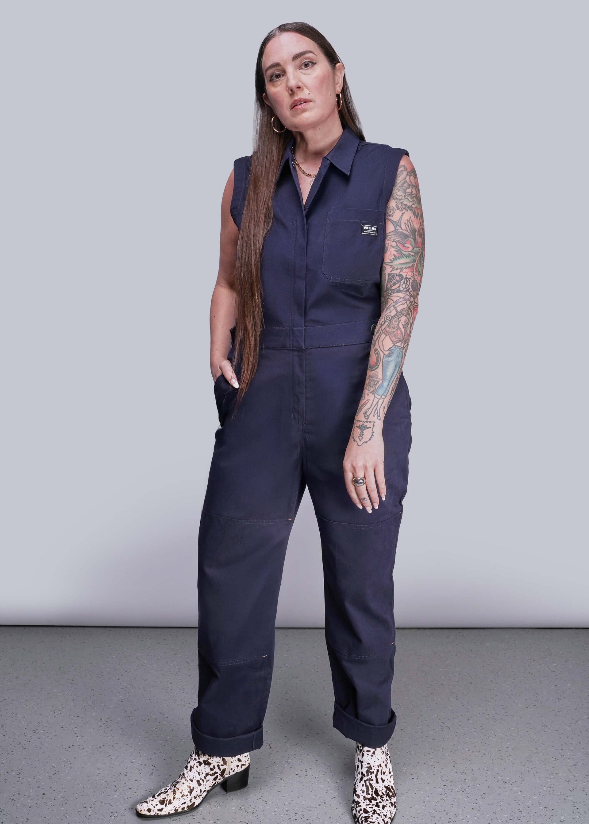 S=Woman wearing a navy blue sleeveless jumpsuit on a plain background