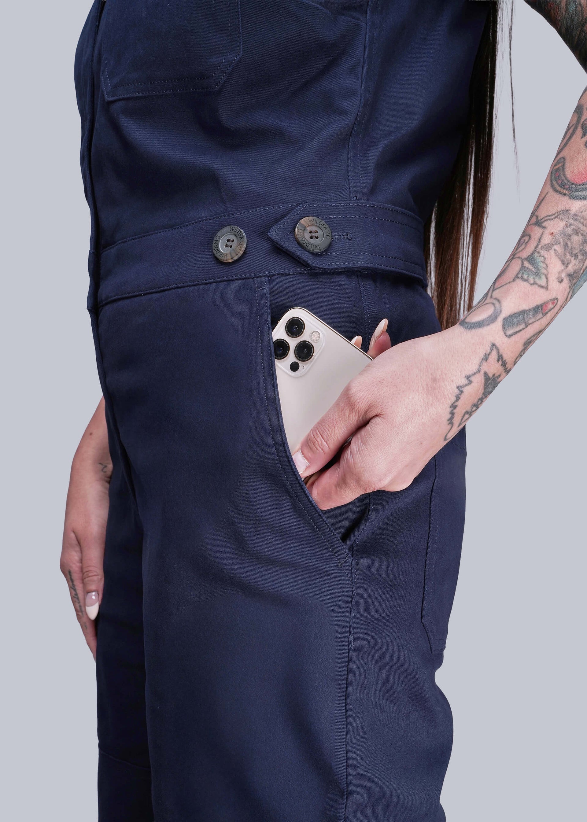 S=Person wearing navy blue pants with a phone in the pocket against a plain background