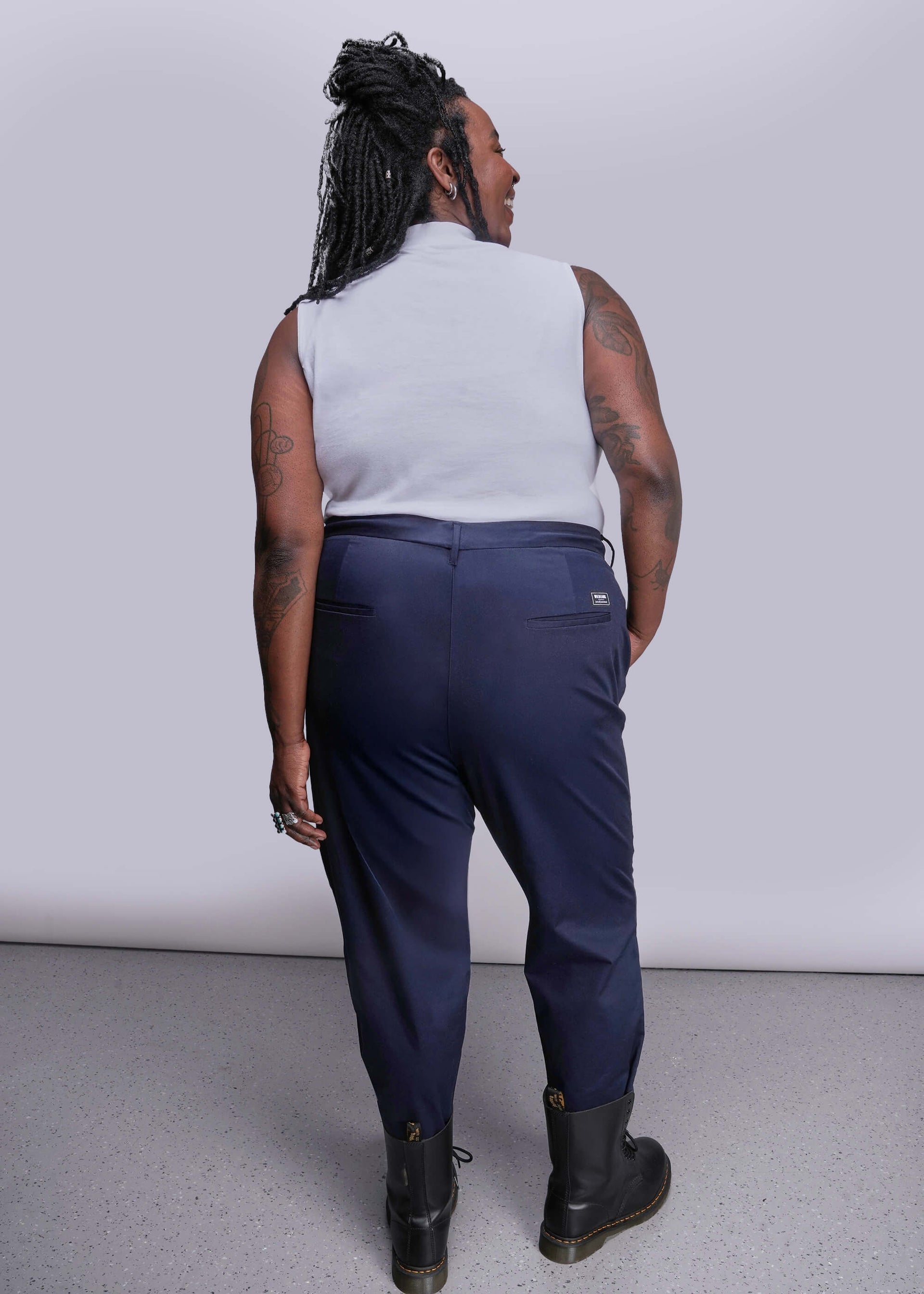 1X=Person wearing navy pants and a white sleeveless top against a plain background