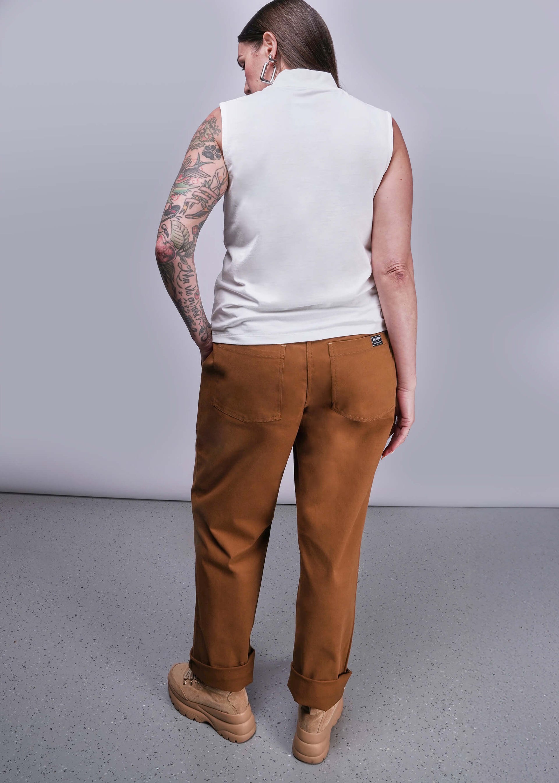 S=Person wearing a white sleeveless shirt and brown pants against a gray background