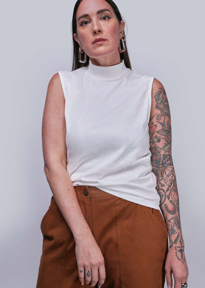 S=Woman wearing a white sleeveless top and brown pants against a plain background
