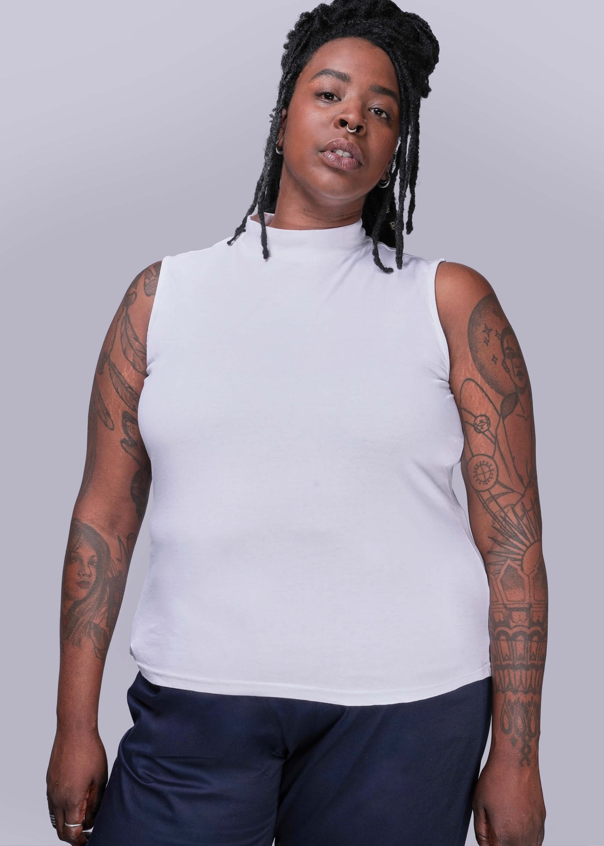 1X=Person wearing a white sleeveless top and dark pants against a plain background