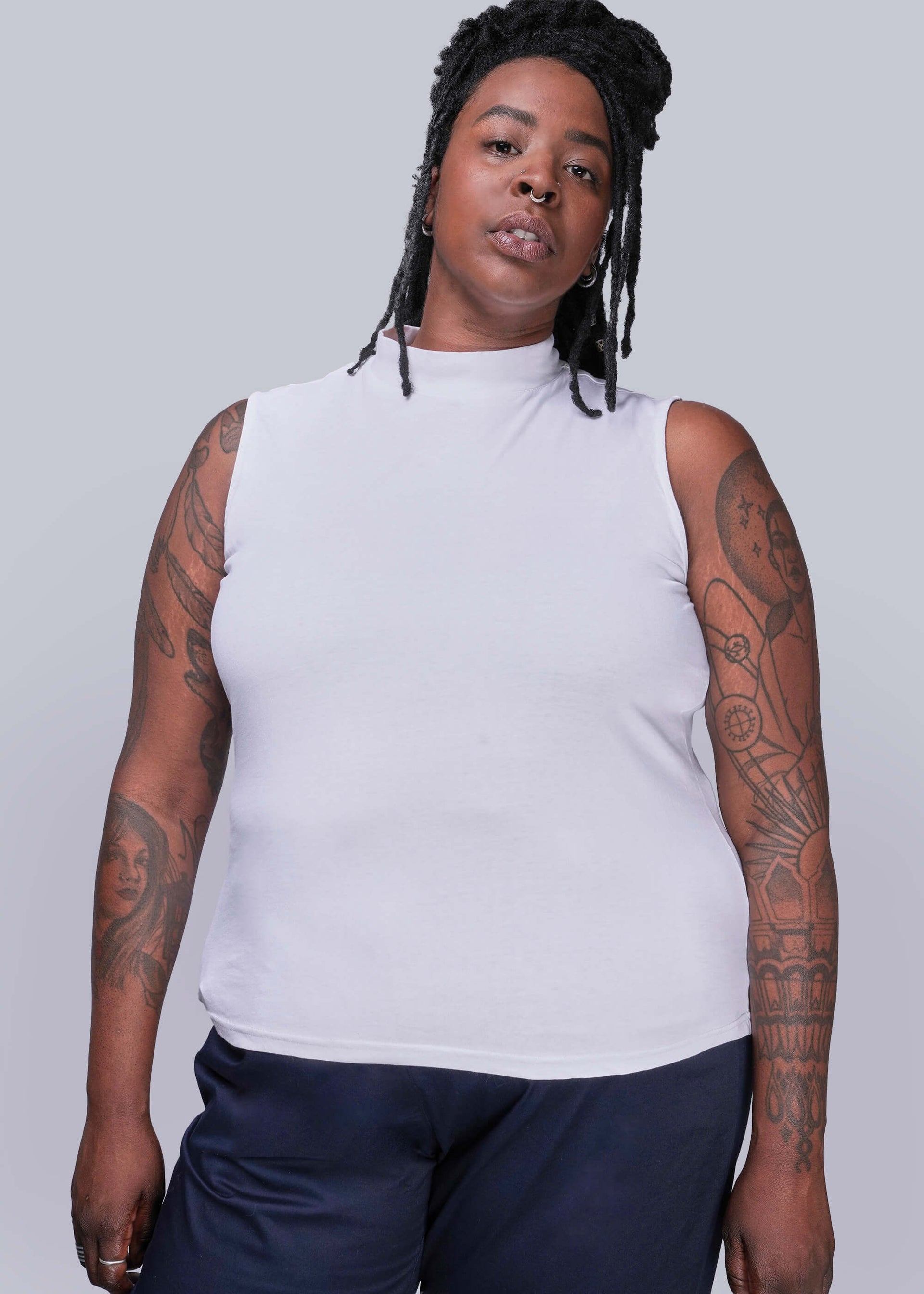 1X=Person wearing a white sleeveless top and dark pants against a plain background