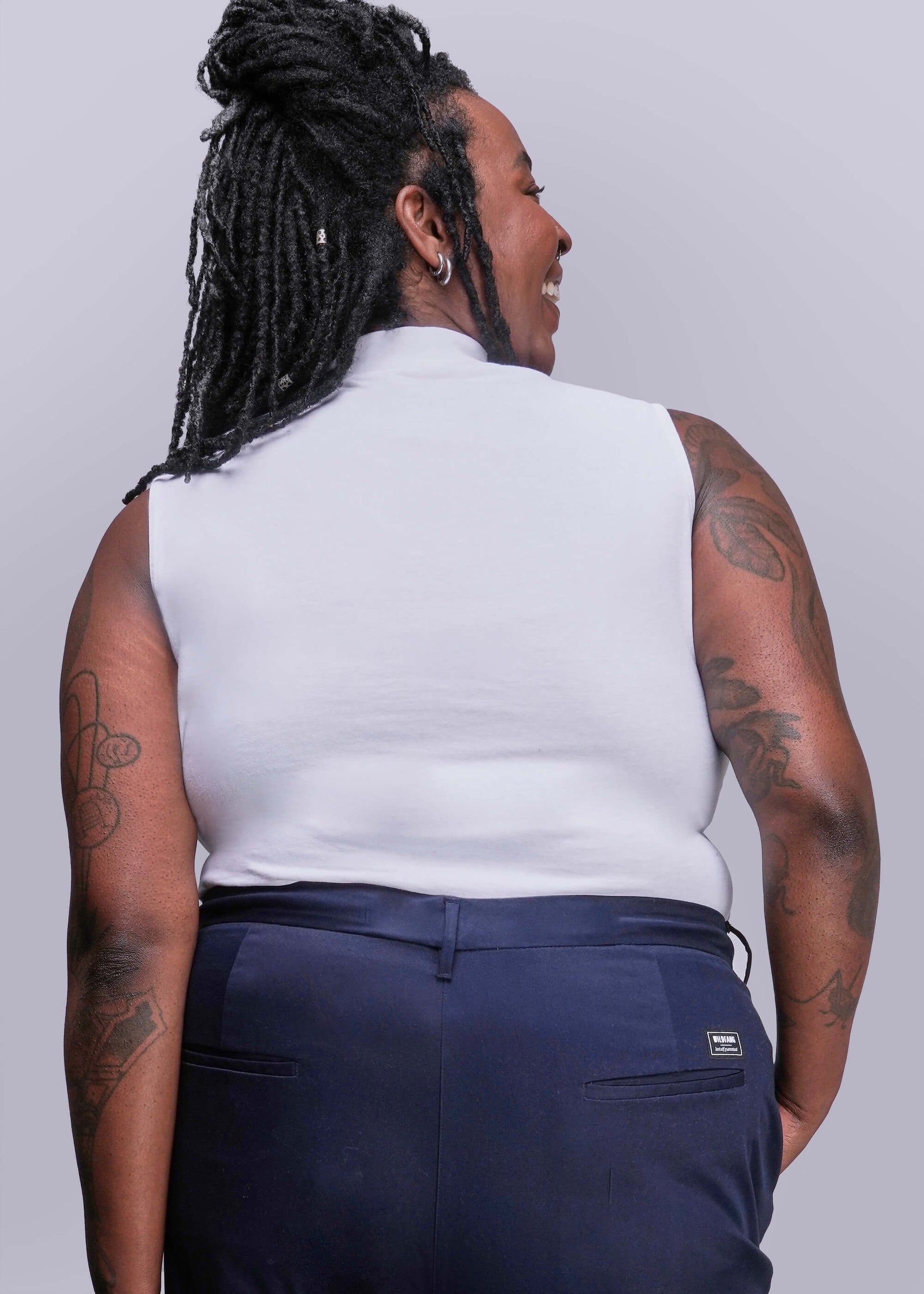 1X=Person wearing a white sleeveless top and navy pants against a plain background