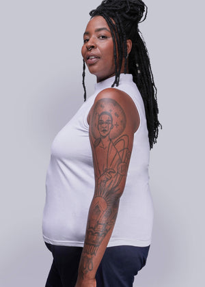 1X=Person wearing a white sleeveless top with tattoos on arms against a gray background