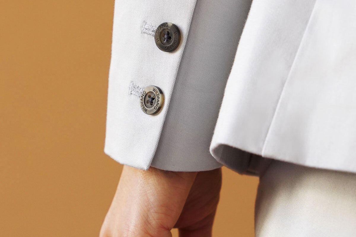 Close up of grey blazer cuff and buttons on orange background.