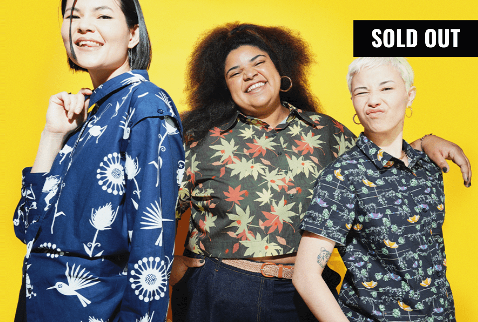 Three models wearing the Laika x Wildfang collab button ups stand in a group in front of yellow background while smiling at camera. An overlay banner on the top right reads SOLD OUT