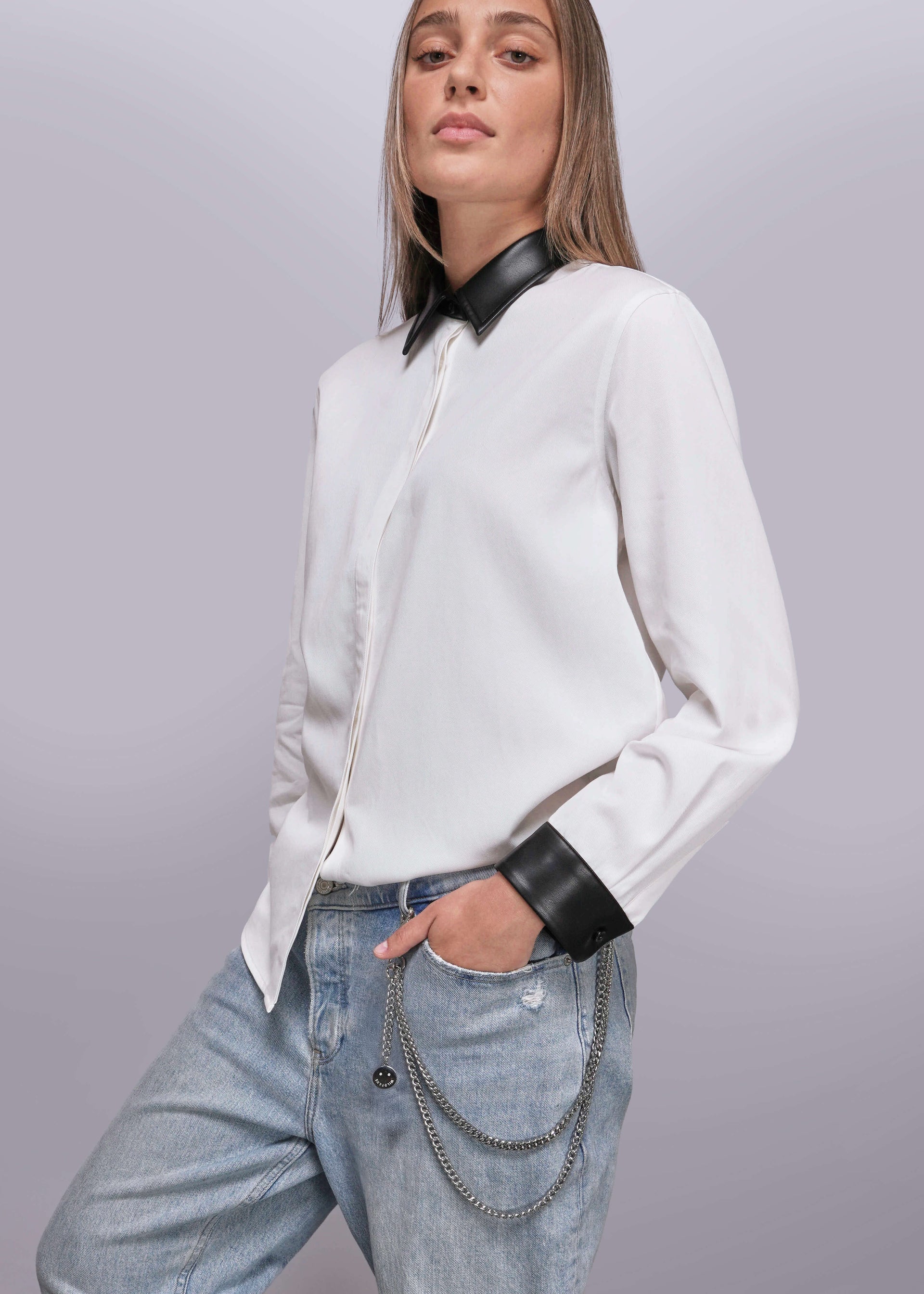 Person wearing a white shirt with black collar and cuffs, paired with blue jeans on a gray background