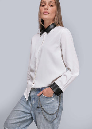 Person wearing a white shirt with black collar and cuffs, paired with blue jeans on a gray background