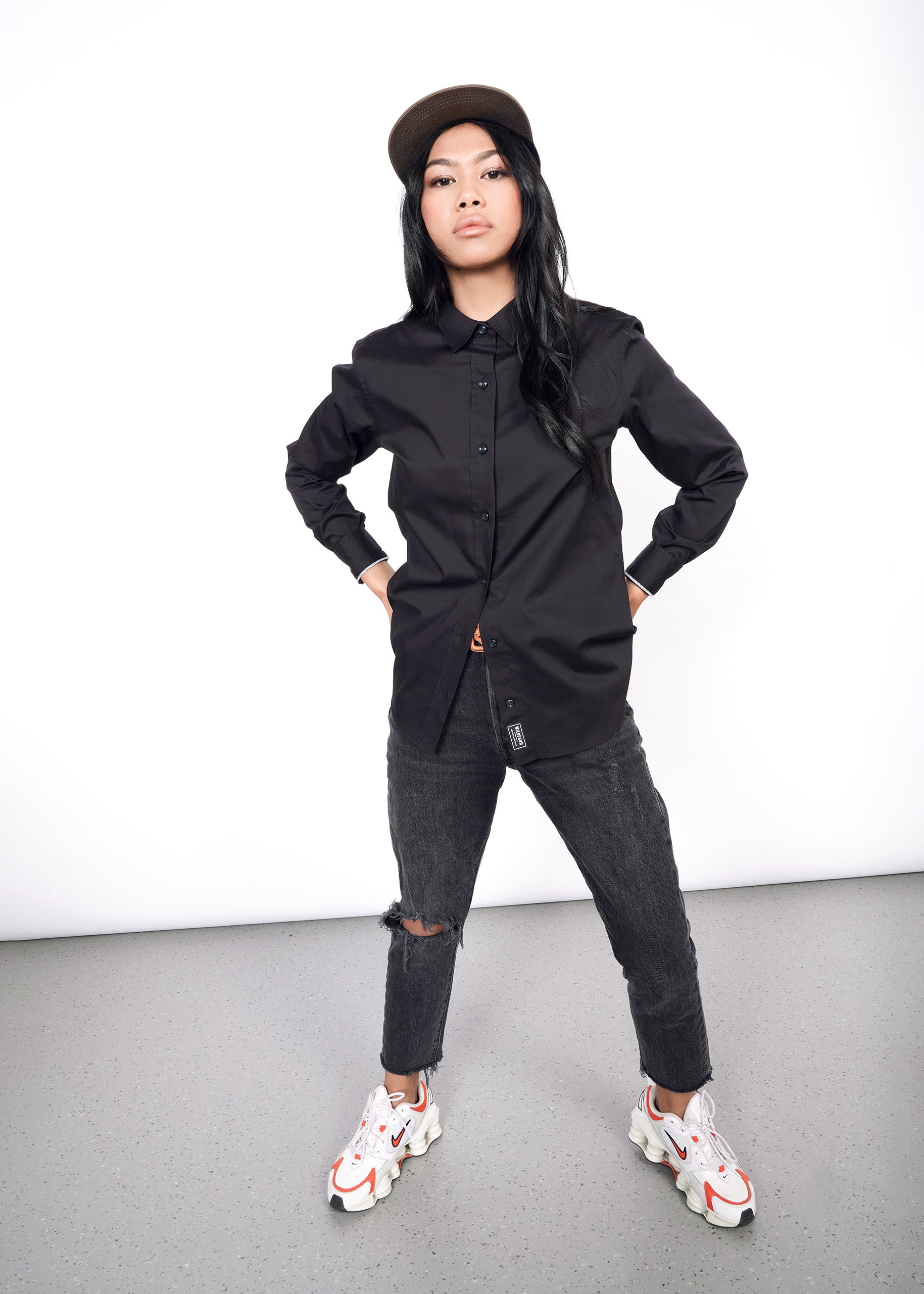 S=Model wearing black long sleeve oxford button up in size XS, buttoned to top and styled with black jeans and sneakers