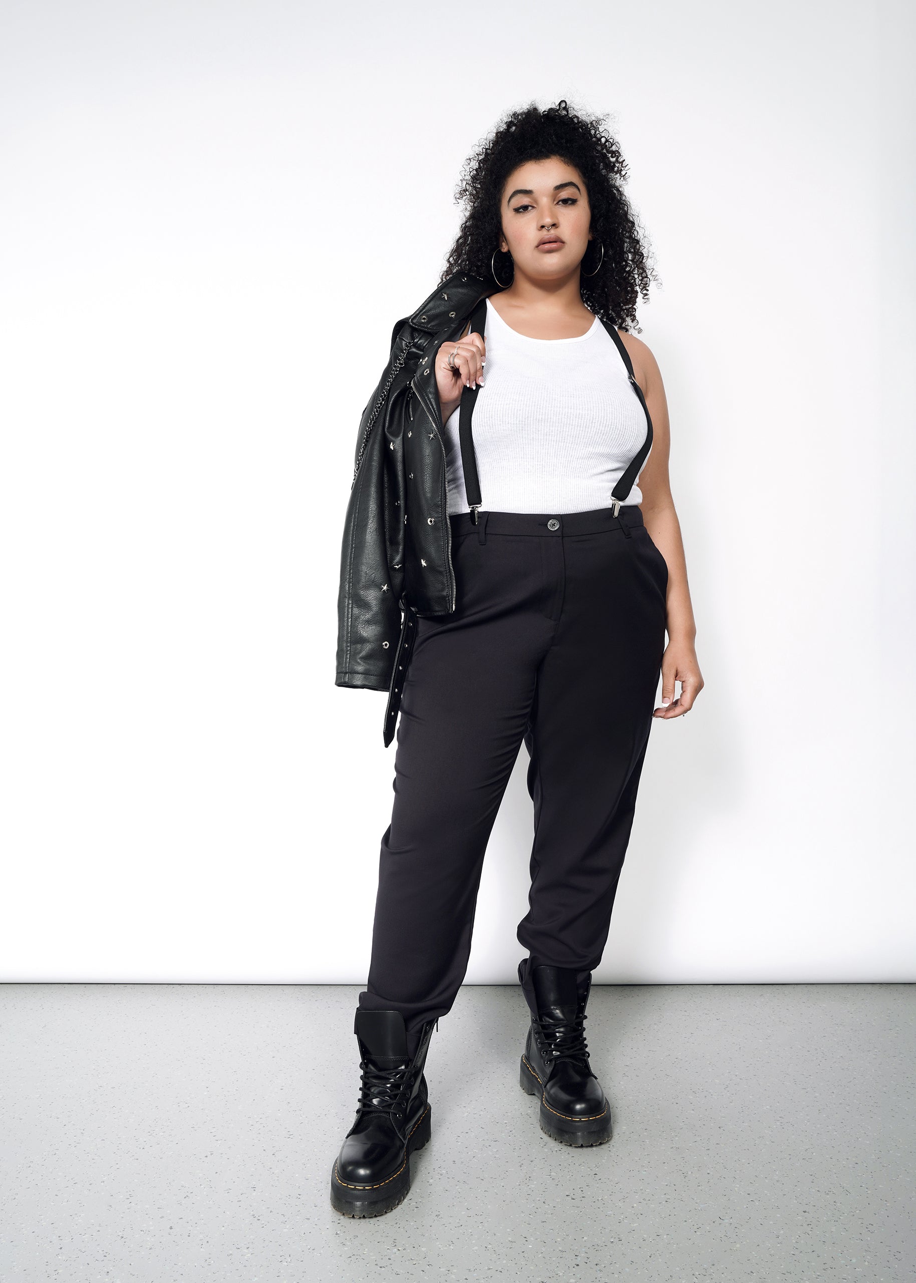 1X=A woman wearing black wildfang pants and a leather jacket. Paired with a white tank, suspenders and doc martens