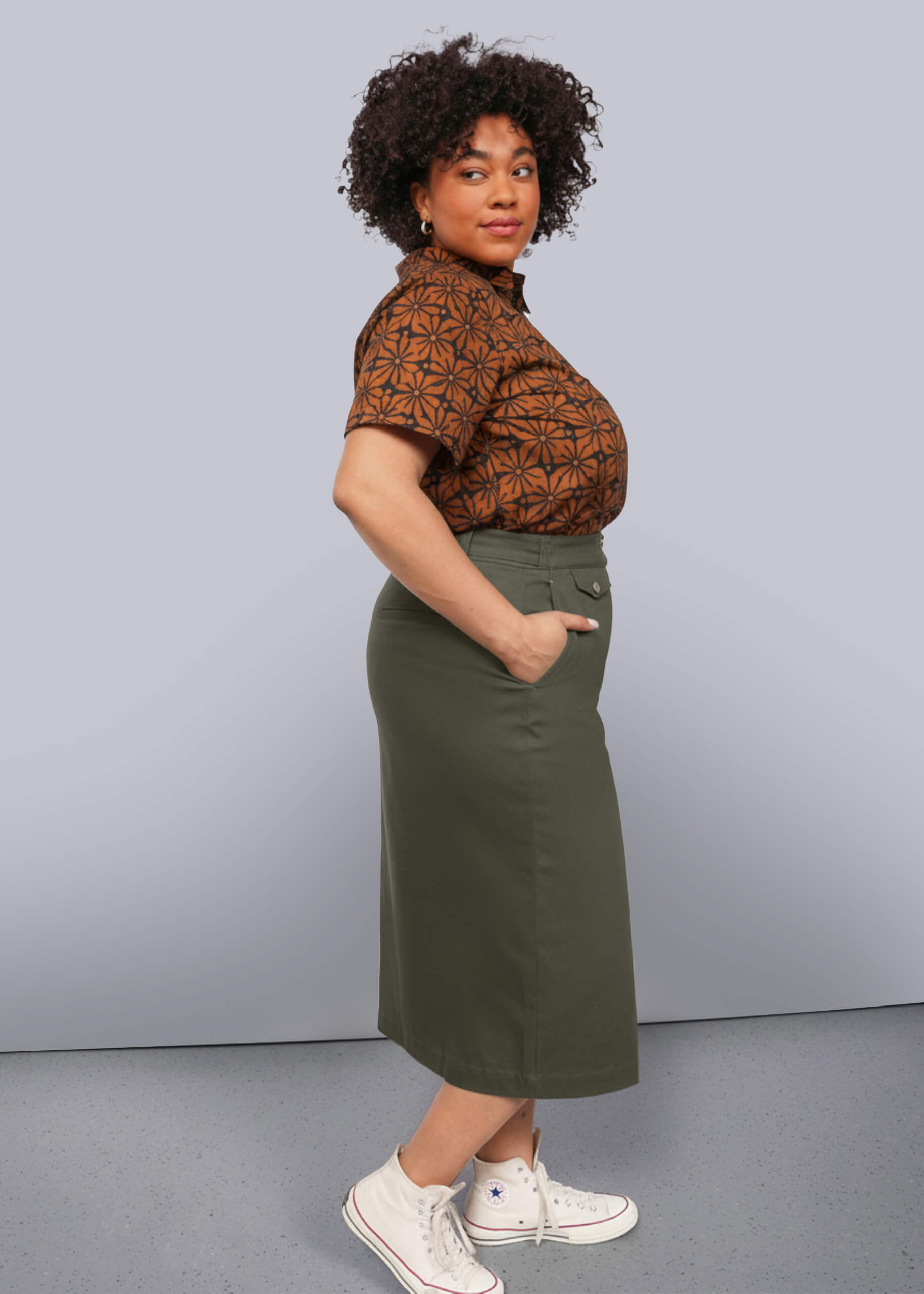 1X=Person wearing a patterned brown shirt and green skirt against a gray background