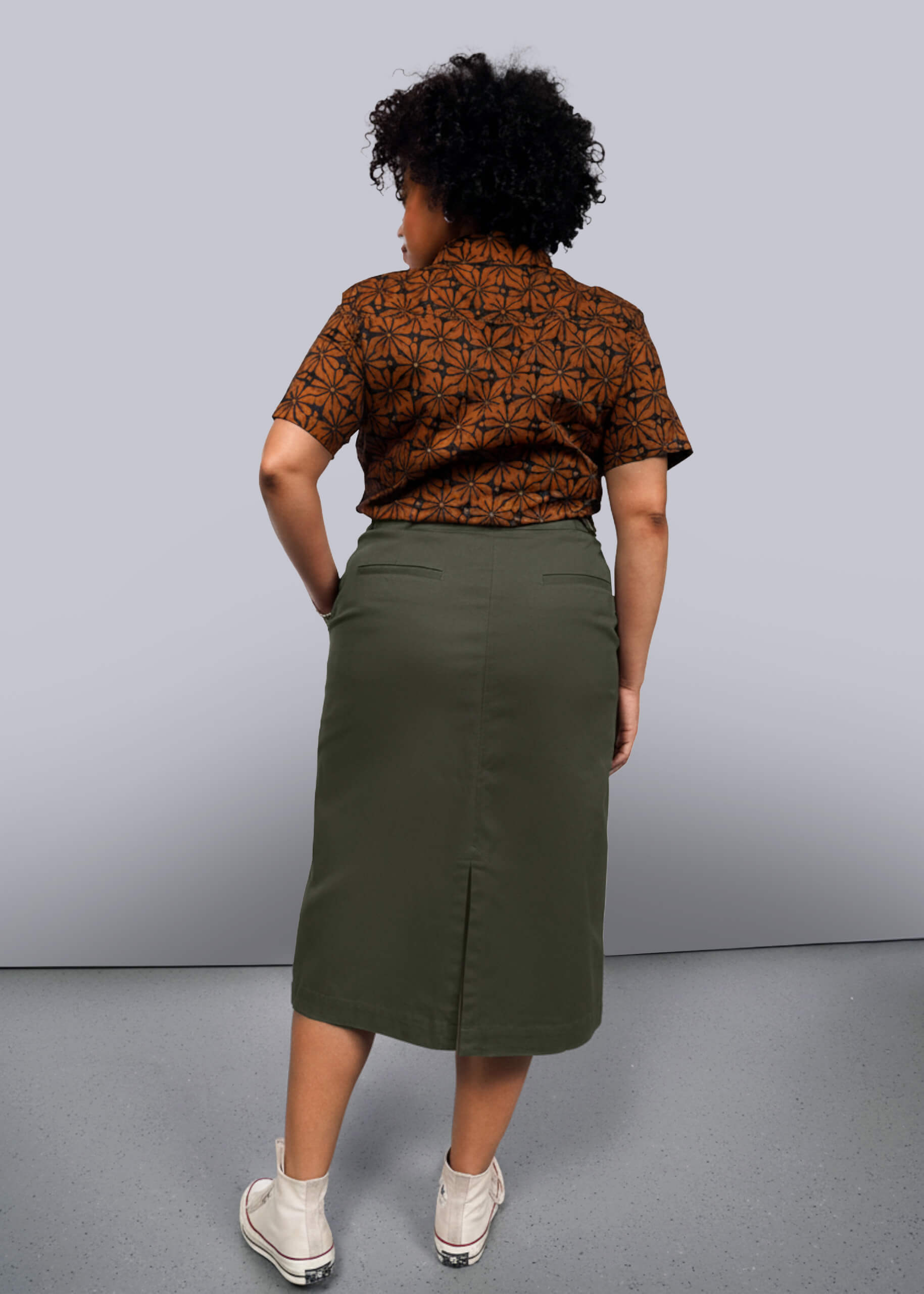 1X=Person wearing a patterned shirt and green skirt against a gray background
