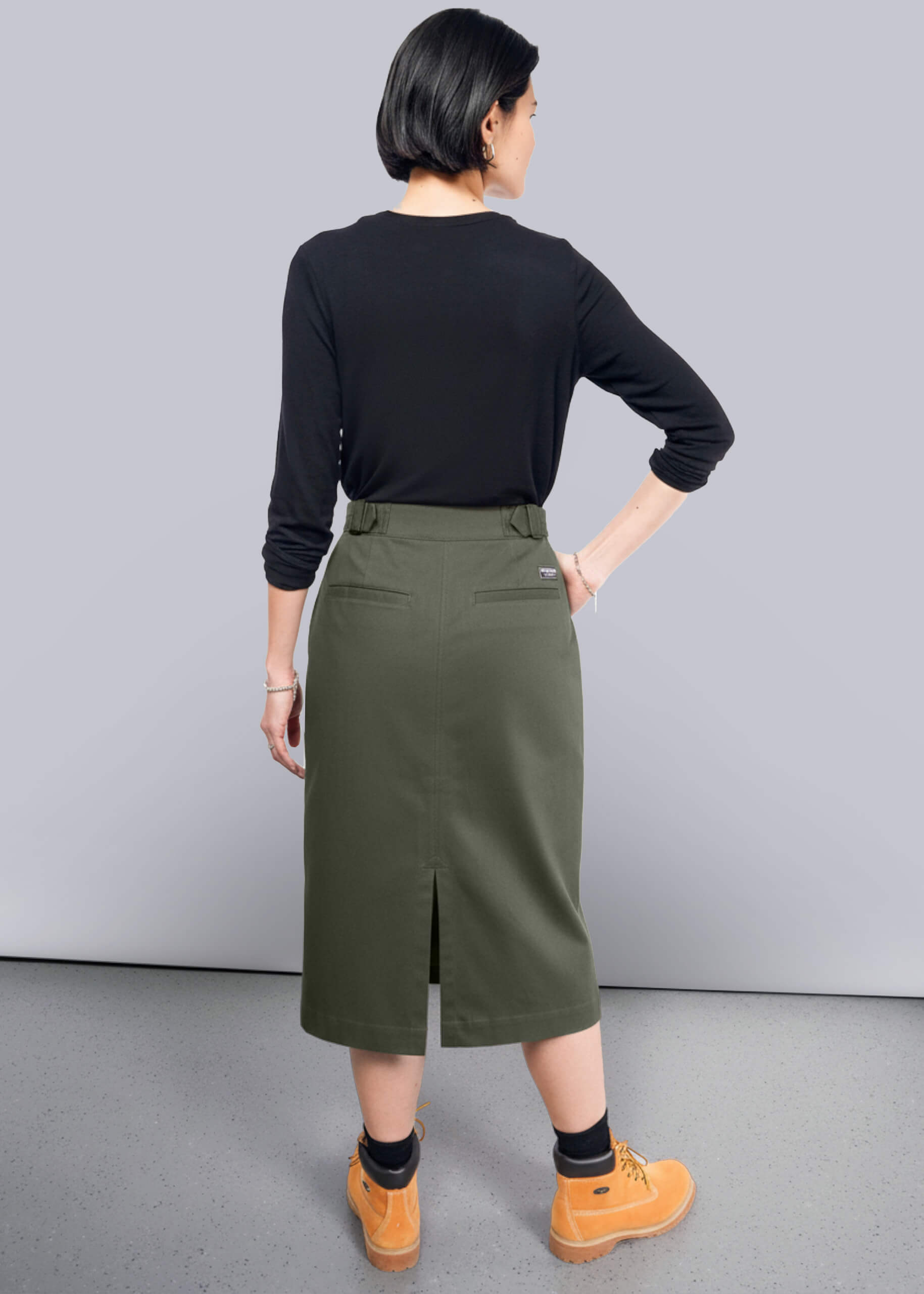 S=Person wearing a black long-sleeve top and green skirt on a gray background