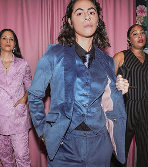 Three people wearing suits from the holiday suiting collection standing in front of pink velvet curtain