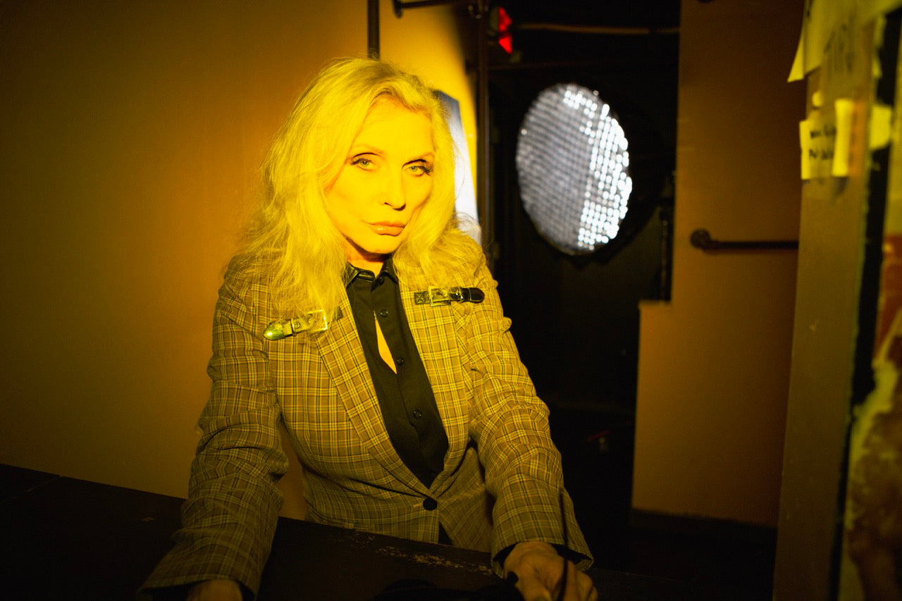 Debbie Harry stands under yellow spotlight wearing the Debbie Harry x Wildfang Blazer