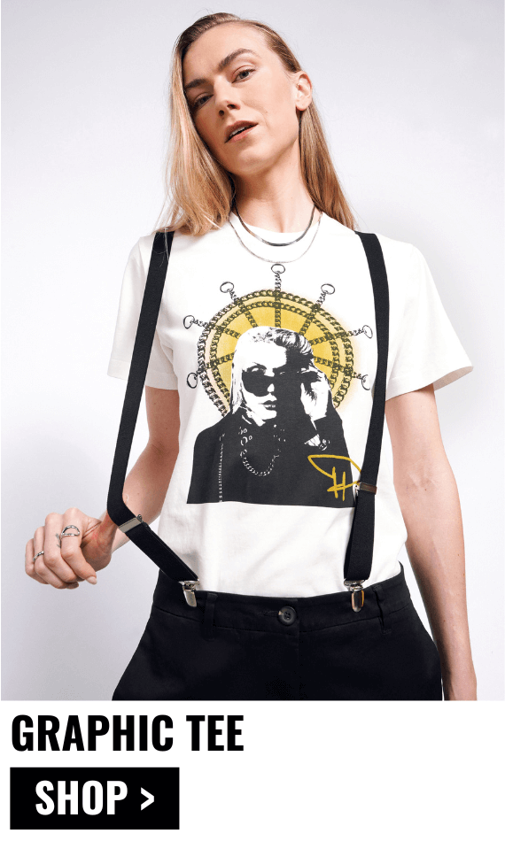 Model with long blonde hair looks at camera wearing suspenders and The Debbie Harry x Wildfang Graphic Tee. Text underneath image and left justified reads GRAPHIC TEE $45 and button underneath reads SHOP.